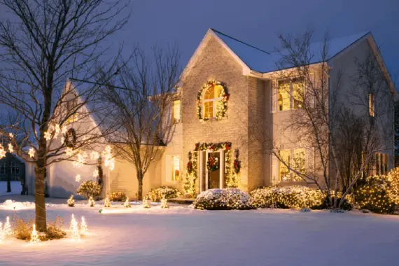 Two-story home covered in Christmas lights and winter snow, showcasing warm holiday curb appeal for winter homebuyers.