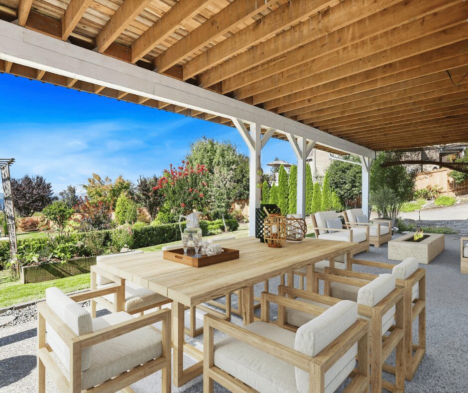 Outdoor covered patio with wooden beams, modern lounge seating, and dining table overlooking a landscaped garden.